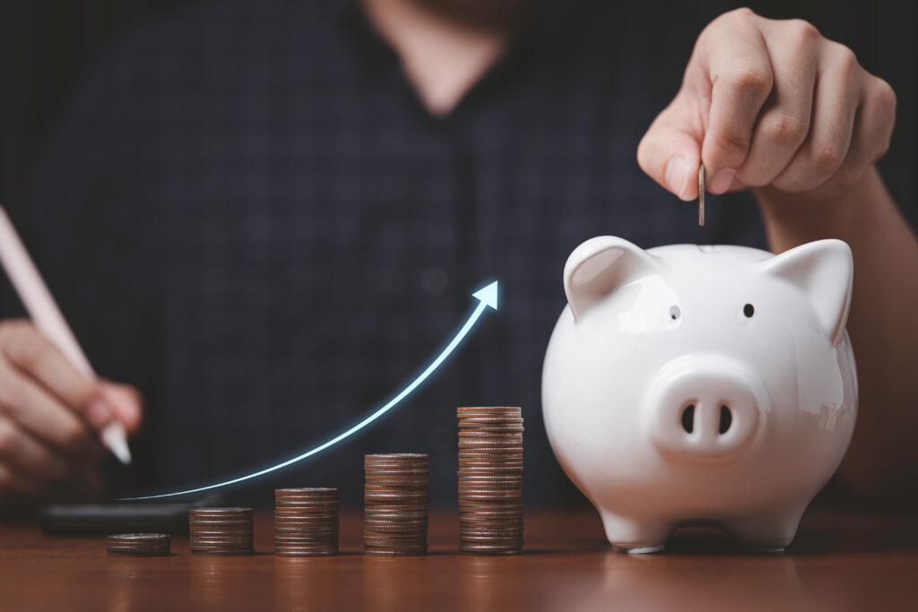 Businessman putting coin to white piggy bank with coins stacking and increasing arrow for growth deposit saving money and increase dividend profit investment concept - ForexMag.cz Dividendové akcie, investování, dividendy