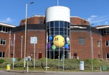 Allwyn, dříve Sazka, loni v ČR zvýšil zisk na 2,1 mld. Kč a tržby na 14,3 mld. Brick office building with a cylindrical glass atrium filled with oversized colorful lottery balls visible through the windows ch:.25 central yellow ball