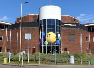 Allwyn, dříve Sazka, loni v ČR zvýšil zisk na 2,1 mld. Kč a tržby na 14,3 mld. Brick office building with a cylindrical glass atrium filled with oversized colorful lottery balls visible through the windows ch:.25 central yellow ball