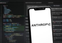 Šéf podniku Anthropic vyzval firmy, aby zpomalily vývoj modelů umělé inteligence Smartphone angled on a blurred code editor background showing the word ANTHROPIC on a white screen.