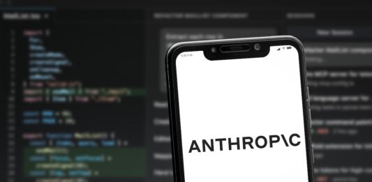 Šéf podniku Anthropic vyzval firmy, aby zpomalily vývoj modelů umělé inteligence Smartphone angled on a blurred code editor background showing the word ANTHROPIC on a white screen.