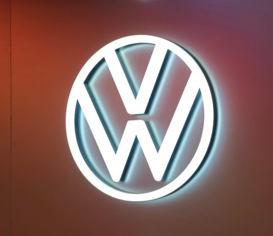 Volkswagen se dělí o výrobu baterií. Rozhodne ekonomika celého koncernu Illuminated Volkswagen logo (white VW circle) on a warm orange wall background.
